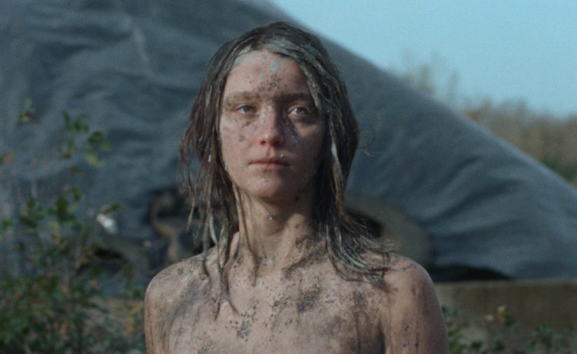 Filmstill zu HER WILL BE DONE. Eine junge Frau im Freien, mit Dreck beschmiert. 