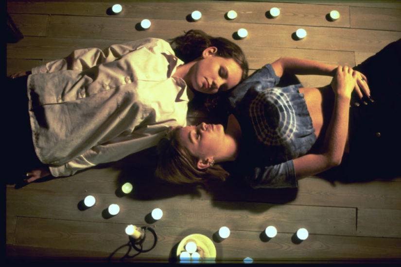 Zwei Frauen liegen mit geschlossenen Augen am Boden umringt von Kerzen.